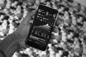 A person's hand holding an iPhone that shows an Apple stock reading.